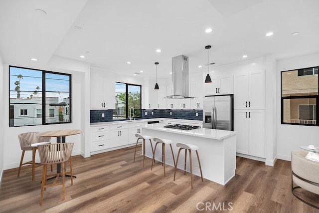 kitchen with a kitchen island, gas cooktop, hanging light fixtures, stainless steel fridge, and wall chimney exhaust hood