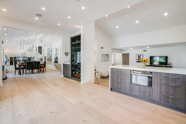 kitchen with vaulted ceiling, dark brown cabinets, and light hardwood / wood-style floors