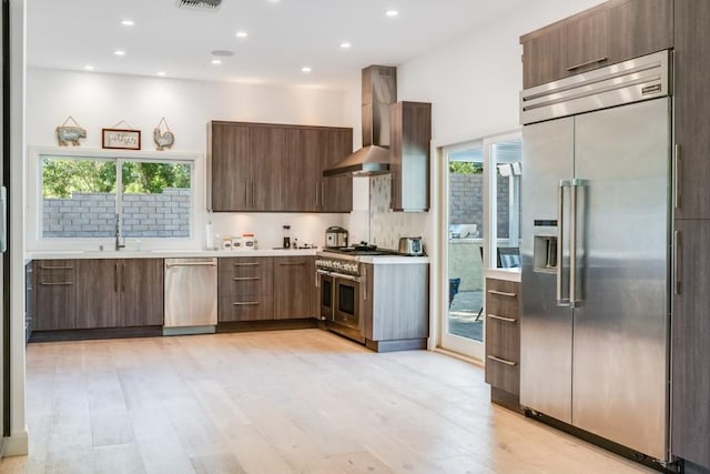 kitchen featuring modern cabinets, a sink, wall chimney range hood, light countertops, and high end appliances