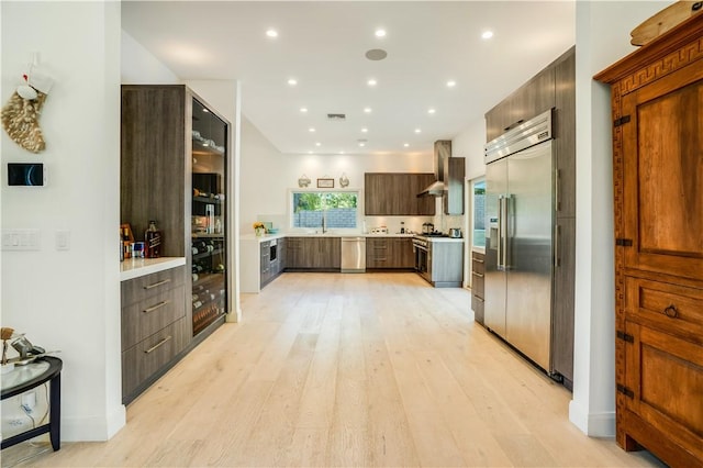 kitchen featuring a sink, stainless steel appliances, light countertops, wall chimney range hood, and modern cabinets