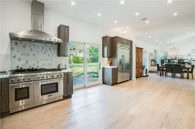 kitchen with tasteful backsplash, dark brown cabinets, high quality appliances, and wall chimney exhaust hood