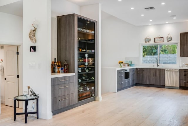 bar featuring dark brown cabinetry, sink, light hardwood / wood-style floors, and dishwasher