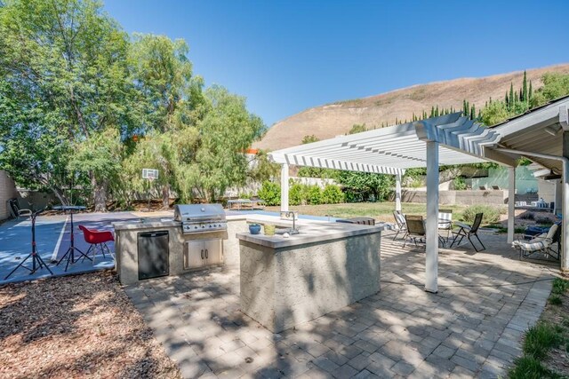 view of patio / terrace with exterior kitchen, a mountain view, area for grilling, and a pergola