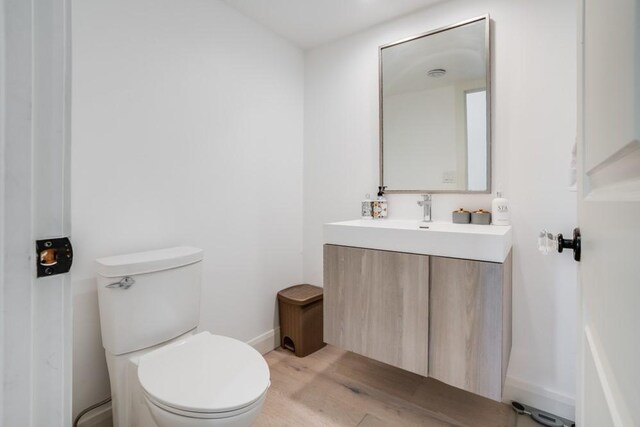 bathroom with baseboards, toilet, wood finished floors, and vanity