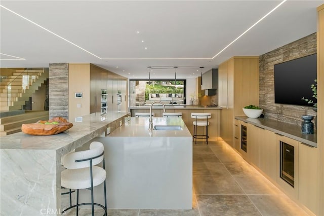 kitchen with a kitchen bar, kitchen peninsula, light brown cabinets, wine cooler, and sink