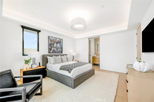 bedroom featuring hardwood / wood-style flooring, a raised ceiling, and ensuite bath