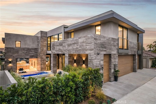 433 Harbor Island Dr, Newport Beach, CA 92660 - back of property at dusk with a balcony, concrete driveway, an attached garage, and stone siding