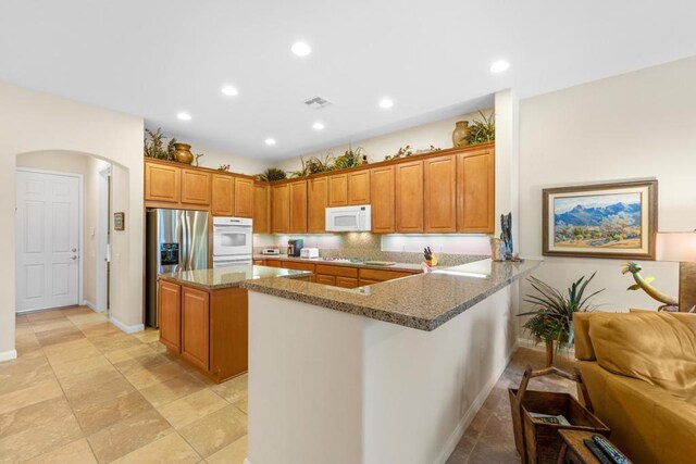 kitchen with kitchen peninsula, a breakfast bar area, white appliances, light stone counters, and a center island