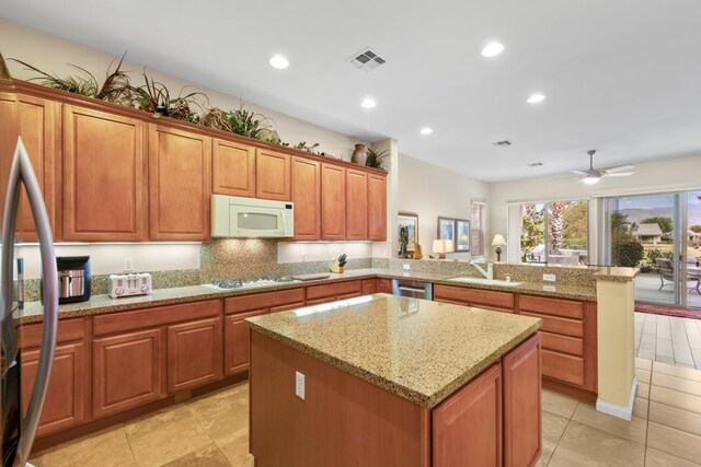 kitchen featuring kitchen peninsula, ceiling fan, stainless steel appliances, light stone countertops, and a kitchen island