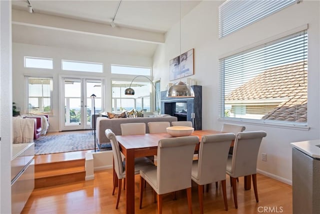 dining space with beam ceiling, light hardwood / wood-style floors, french doors, and a high ceiling