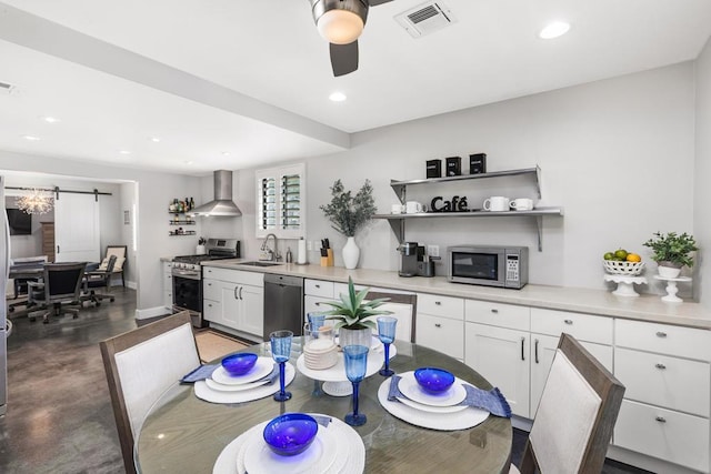 kitchen with appliances with stainless steel finishes, white cabinetry, sink, ceiling fan, and wall chimney range hood