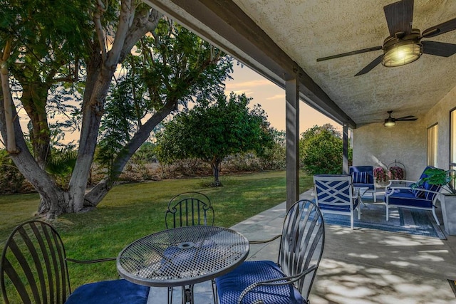 patio terrace at dusk with ceiling fan, an outdoor living space, and a lawn