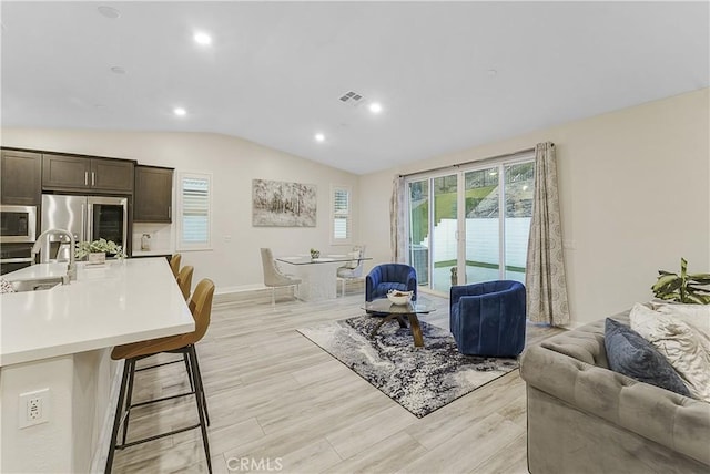 living room with lofted ceiling, sink, and light wood-type flooring