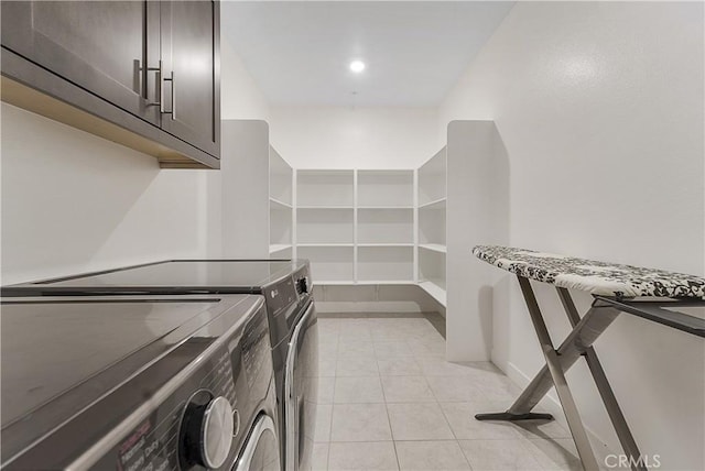 clothes washing area featuring cabinets, light tile patterned floors, and washer and clothes dryer