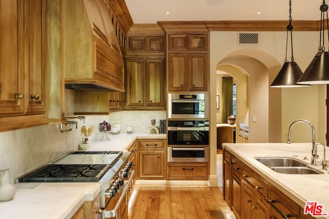 kitchen with tasteful backsplash, pendant lighting, sink, light wood-type flooring, and stainless steel appliances