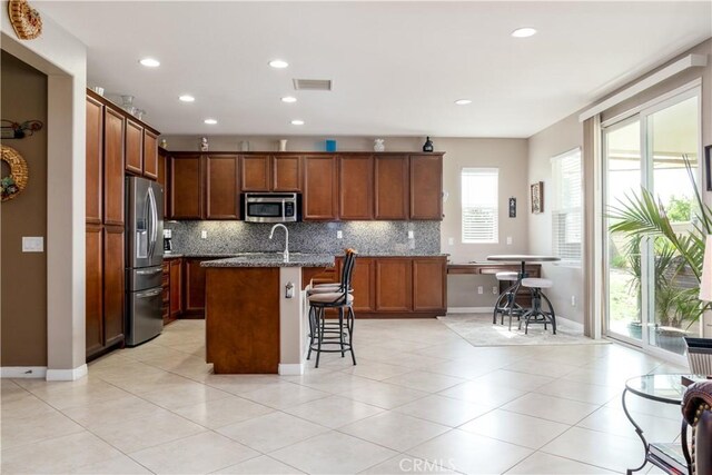 kitchen with appliances with stainless steel finishes, decorative backsplash, sink, a kitchen island with sink, and a breakfast bar area