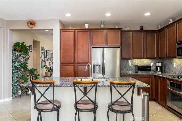 kitchen with appliances with stainless steel finishes, dark stone countertops, and a kitchen island with sink