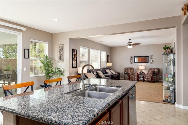 kitchen with ceiling fan, light colored carpet, stainless steel dishwasher, sink, and an island with sink