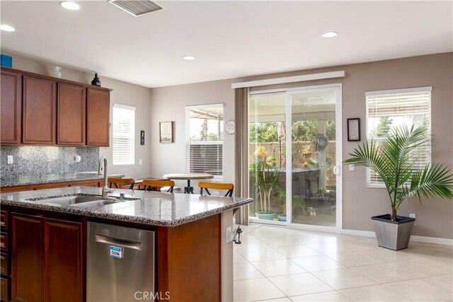 kitchen featuring light tile patterned floors, tasteful backsplash, dark stone countertops, stainless steel dishwasher, and sink