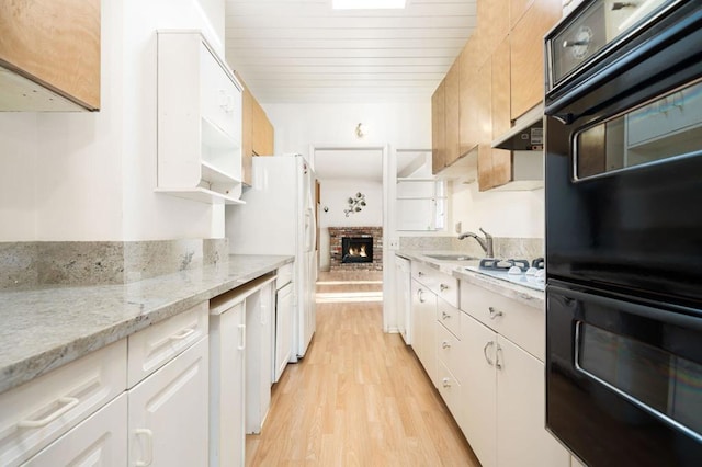 kitchen with a brick fireplace, light hardwood / wood-style flooring, white cabinets, black double oven, and light stone counters