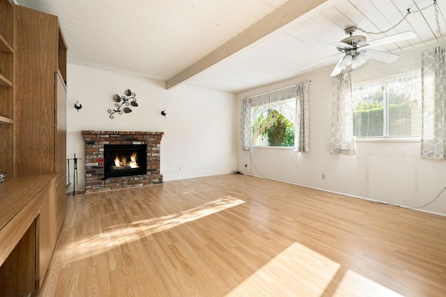 unfurnished living room featuring a brick fireplace, ceiling fan, beamed ceiling, and light hardwood / wood-style floors