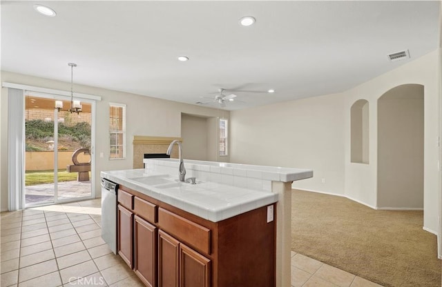 kitchen featuring an island with sink, tile counters, light colored carpet, dishwasher, and sink