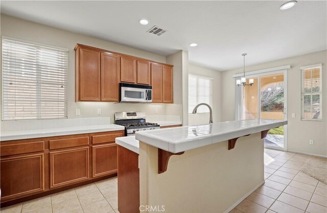 kitchen featuring an island with sink, gas stove, plenty of natural light, and decorative light fixtures