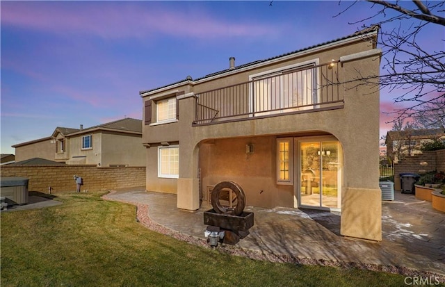 back house at dusk featuring a lawn, cooling unit, a balcony, and a patio