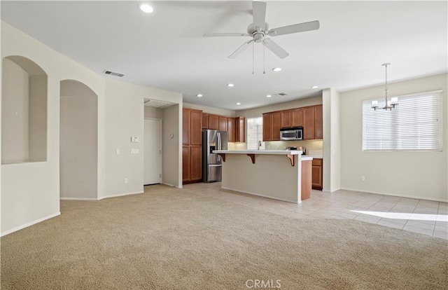 kitchen with appliances with stainless steel finishes, a center island, light carpet, a kitchen breakfast bar, and hanging light fixtures