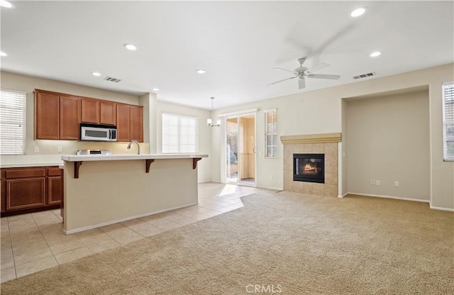 kitchen with decorative light fixtures, light carpet, a fireplace, an island with sink, and a breakfast bar area