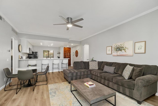 living room featuring ceiling fan, sink, light hardwood / wood-style flooring, and crown molding