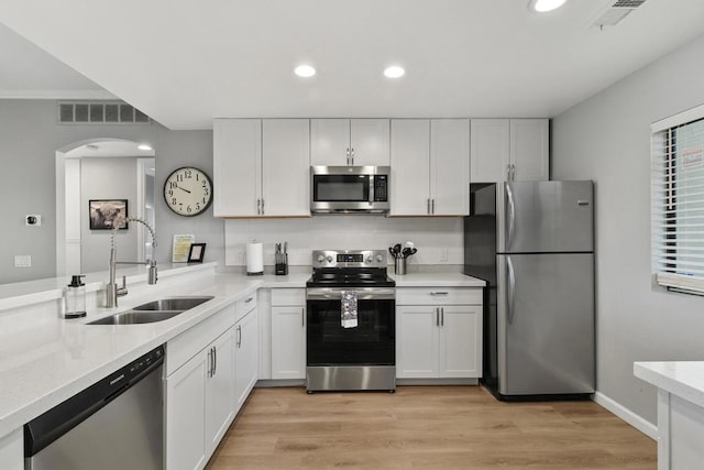 kitchen featuring light stone countertops, white cabinets, appliances with stainless steel finishes, sink, and light wood-type flooring