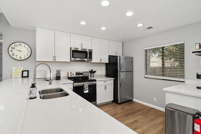 kitchen featuring white cabinetry, hardwood / wood-style flooring, appliances with stainless steel finishes, light stone counters, and sink