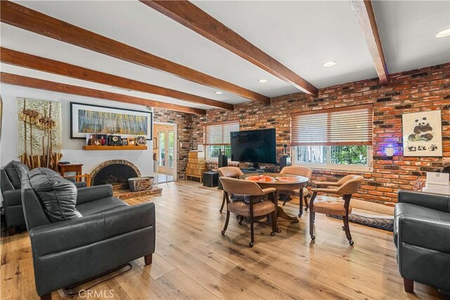 living room with a brick fireplace, brick wall, beam ceiling, and light hardwood / wood-style flooring