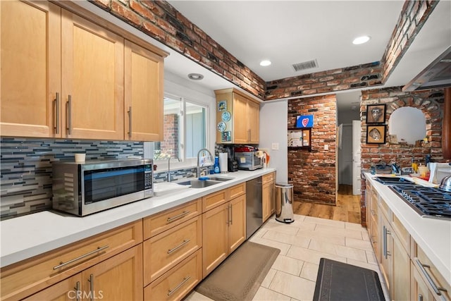 kitchen with sink, light brown cabinets, stainless steel appliances, light tile patterned floors, and brick wall