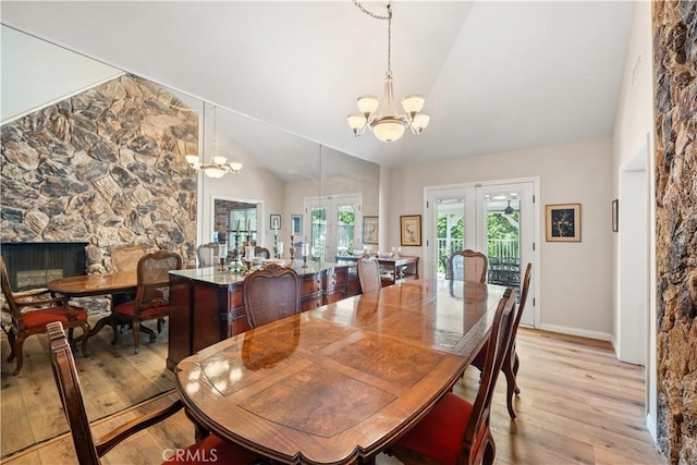 dining space featuring french doors, a stone fireplace, a chandelier, vaulted ceiling, and light hardwood / wood-style flooring