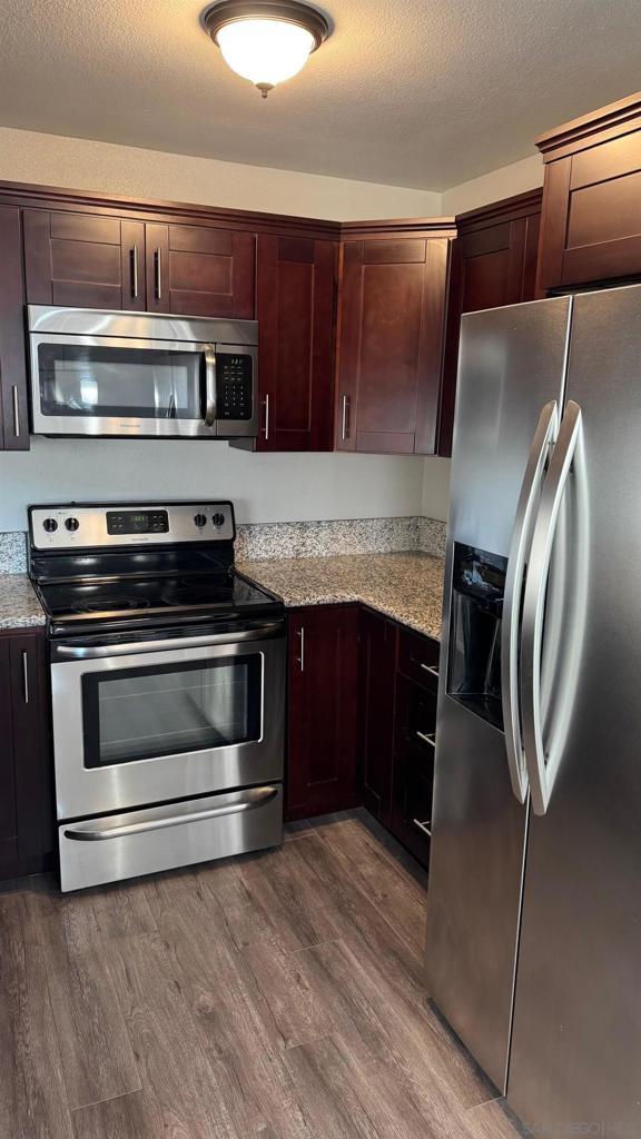 kitchen with a textured ceiling, dark wood-type flooring, stainless steel appliances, and light stone countertops