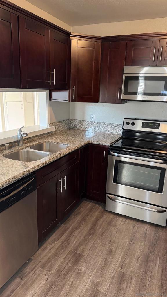 kitchen featuring light stone countertops, sink, wood-type flooring, and appliances with stainless steel finishes