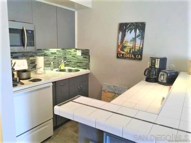 kitchen featuring tile countertops, gray cabinets, tasteful backsplash, range, and sink