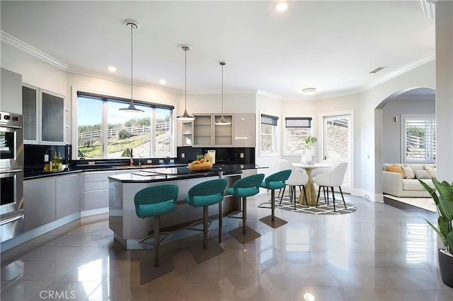 kitchen with hanging light fixtures, a breakfast bar, backsplash, and ornamental molding