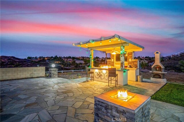 patio terrace at dusk with an outdoor fireplace, a fire pit, and area for grilling