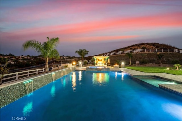 pool at dusk featuring an in ground hot tub and pool water feature