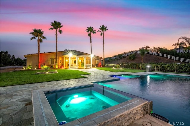 pool at dusk with an in ground hot tub, a yard, and a patio