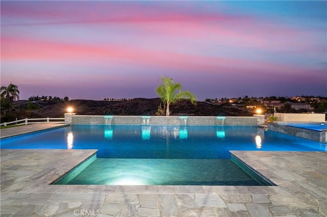 pool at dusk with pool water feature and a patio