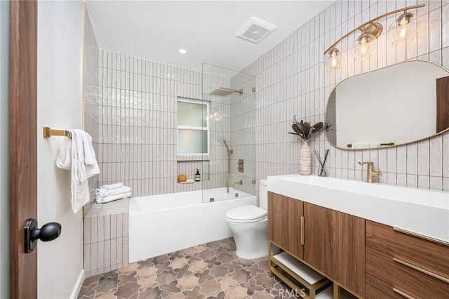 full bathroom featuring toilet, tile walls, vanity, and tiled shower / bath combo