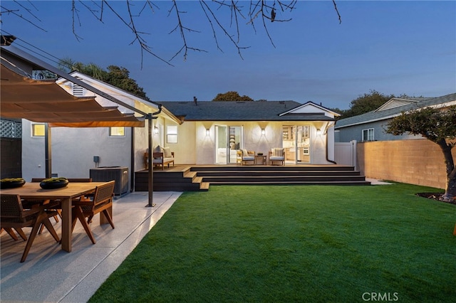 back house at dusk with a deck, cooling unit, a lawn, and a pergola