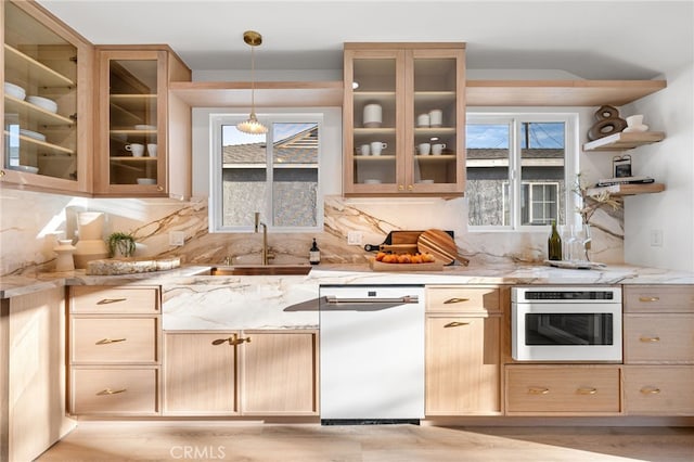 kitchen featuring light brown cabinets, oven, pendant lighting, light stone counters, and dishwashing machine