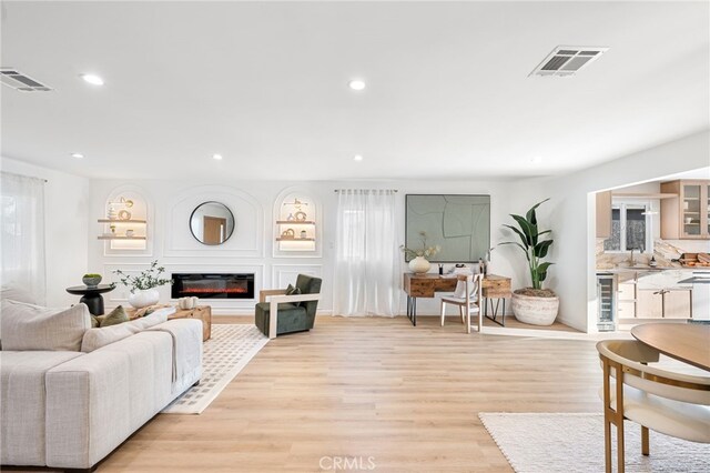 living room with wine cooler, sink, a wealth of natural light, and light hardwood / wood-style floors