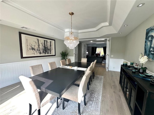 dining room with crown molding, light hardwood / wood-style flooring, a raised ceiling, and a chandelier