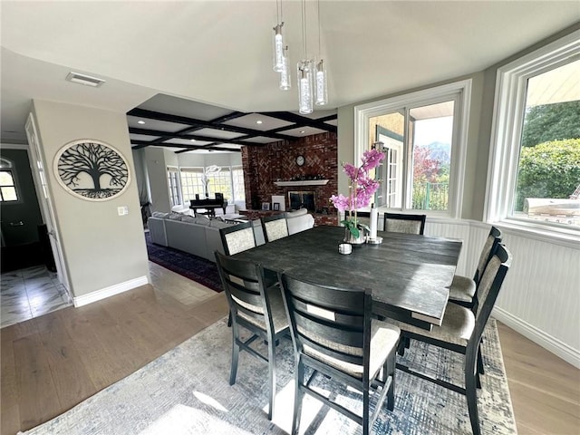 dining space with beam ceiling, a notable chandelier, a fireplace, and light hardwood / wood-style flooring